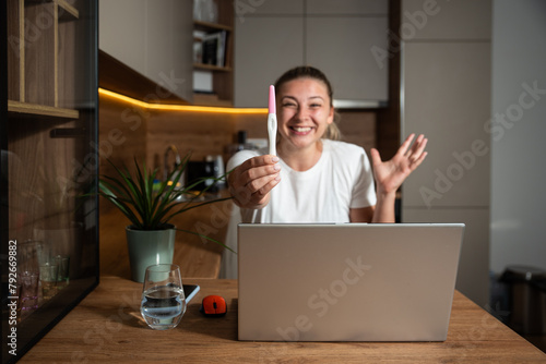 Young happy woman or girl call her boyfriend or husband on video call via laptop to show him positive result on pregnancy test. Positive euphoric female calling mom to tell she is pregnant.