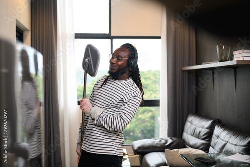 Cheerful African man dancing and singing while cleaning living room