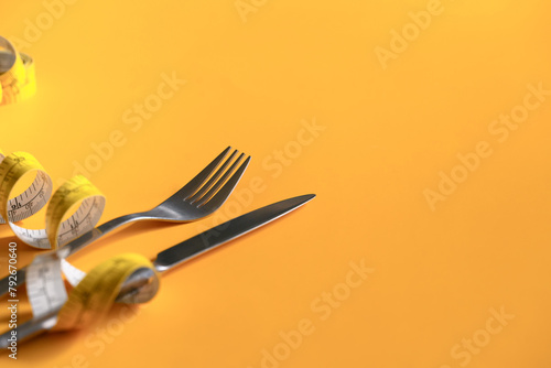 Measuring tape around fork and knife on yellow background. Weight loss and healthy concept