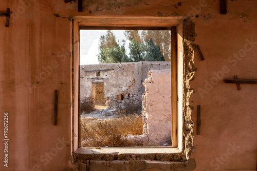 View through a broken window of ruined buildings and courtyard in Al Jazirah Al Hamra haunted town in Ras Al Khaimah, United Arab Emirates.