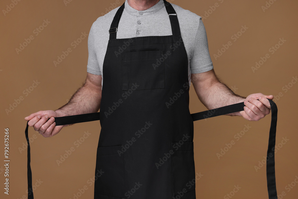 Obraz premium Man wearing kitchen apron on brown background, closeup. Mockup for design