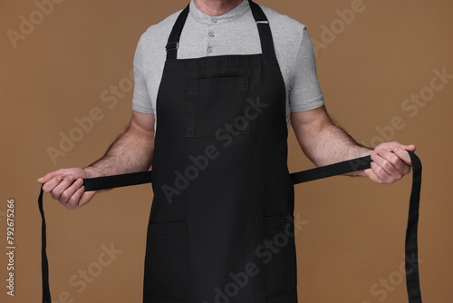 Man wearing kitchen apron on brown background, closeup. Mockup for design © New Africa