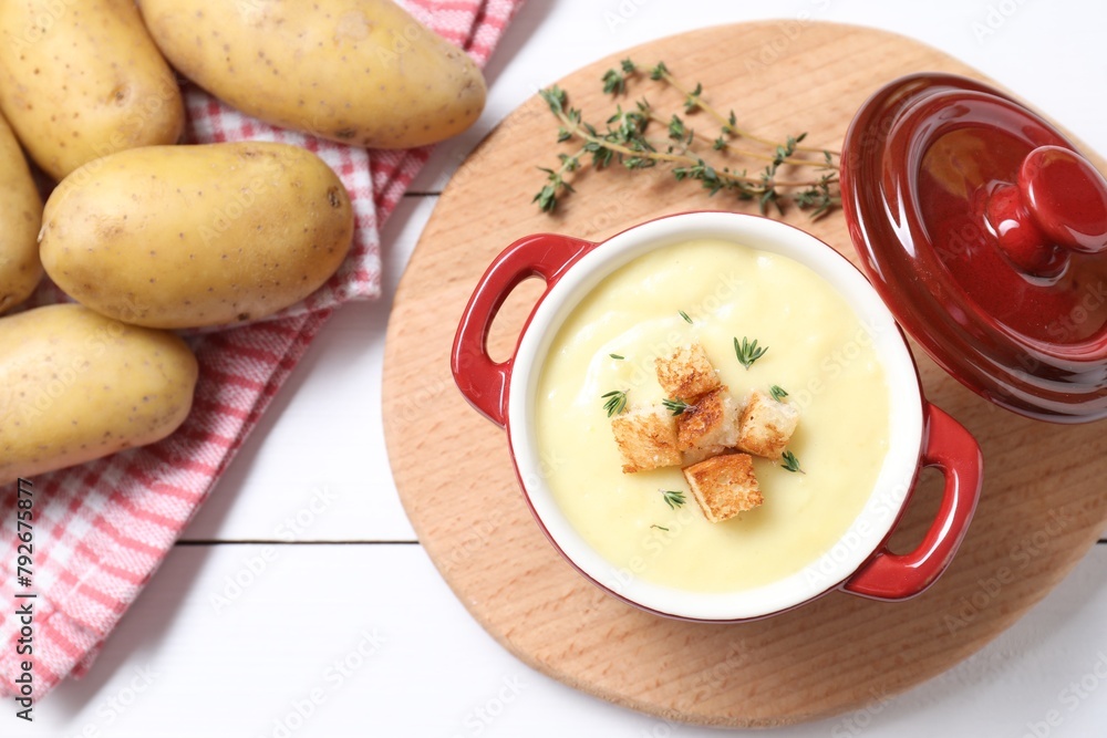 Tasty potato soup with croutons in ceramic pot and ingredients on white wooden table, flat lay
