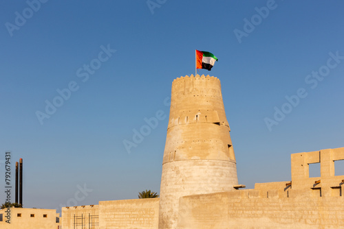 Stone arabic watchtower with waving United Arab Emirates National Flag in Al Jazirah Al Hamra haunted town in Ras Al Khaimah.