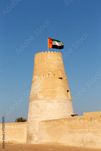 Stone arabic watchtower with waving United Arab Emirates National Flag in Al Jazirah Al Hamra haunted town in Ras Al Khaimah.