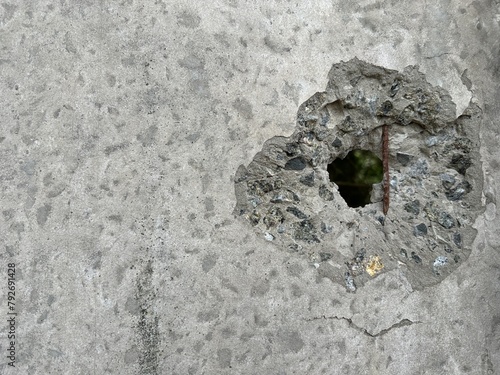 The concrete wall is pierced by a bullet. Background texture: a hole in the concrete from a gunshot. Traces of shelling on the wall, close-up.