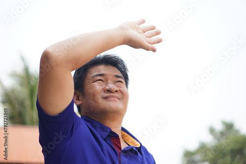Asian man is outdoor, face up to sky, hand over his head, feel hot and unwell. Concept, standing outdoor in hot weather is risk to heat stroke symptom. Global warming.                     