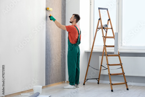 Man hanging stylish gray wallpaper in room