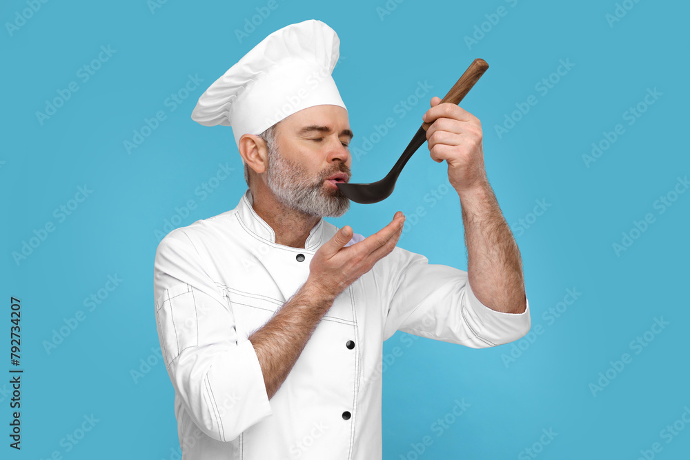 Chef in uniform tasting something on light blue background Chef in uniform tasting something on light blue background