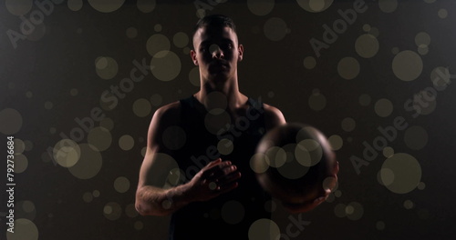 Image of caucasian basketball player throwing ball and spots of light on black background