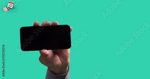 Image of hand holding smartphone on green background