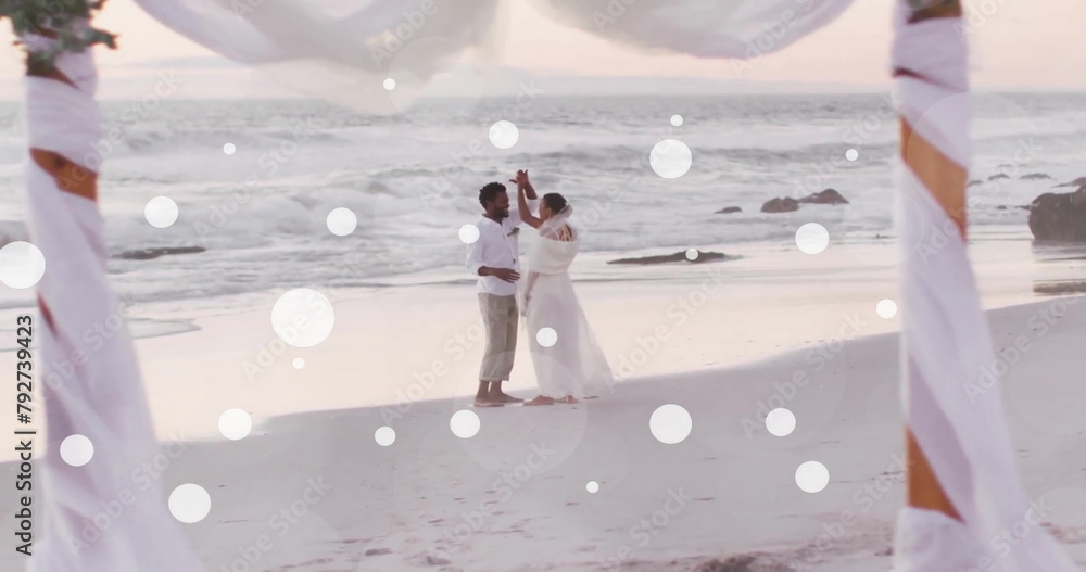 Obraz premium Image of white spots over african american bride and groom dancing on beach at wedding