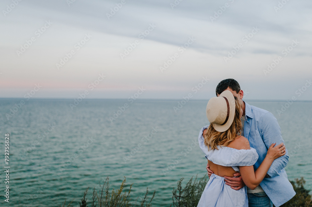 Couple in love standing and kissing on edge of cliff on seashore. Man and woman kiss and embrace on sand sea spending time together. Female and male on beach ocean and enjoying sunny summer day
