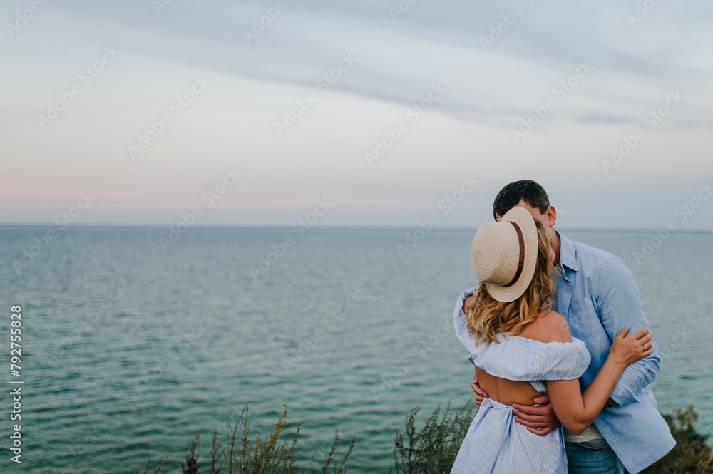 Couple in love standing and kissing on edge of cliff on seashore. Man and woman kiss and embrace on sand sea spending time together. Female and male on beach ocean and enjoying sunny summer day Couple in love standing and kissing on edge of cliff on seashore. Man and woman kiss and embrace on sand sea spending time together. Female and male on beach ocean and enjoying sunny summer day