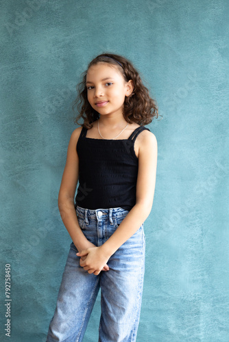Vertical view of cute mixed race nine-year old smiling girl standing against blue background