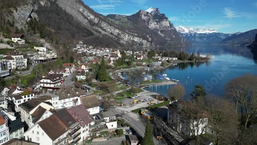 Drone clip showing white buildings in small lakeside village in Switzerland, with snowy mountains in the background photo