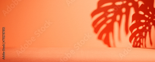Tropical summer background with monstera palm leaf shadow on orange wall. Empty room for luxury brand product placement mockup.