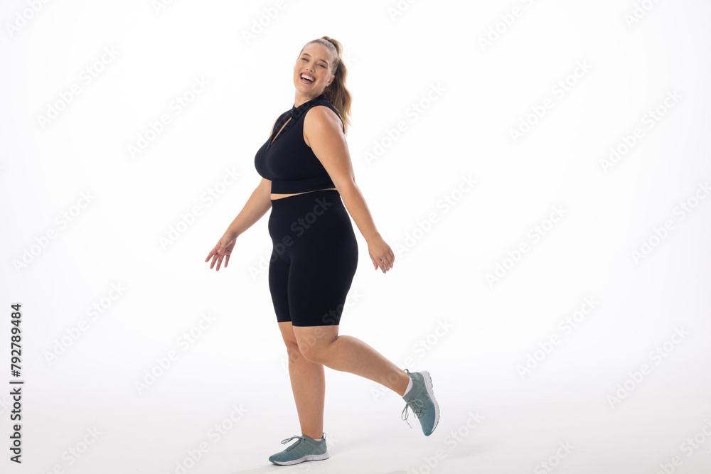 Caucasian young female plus size model on white background is laughing and walking, copy space