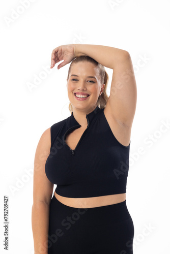 Smiling Caucasian plus-size model poses, hand on head, against white background
