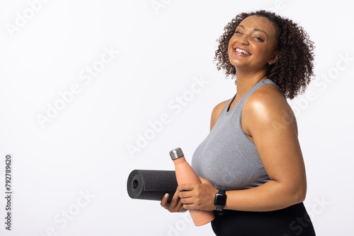A biracial young female plus size model holds yoga mat and water bottle, copy space