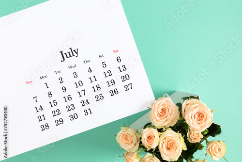 Flat lay of paper desk calendar for July 2024, top view. White beautiful roses on a pastel mint background.