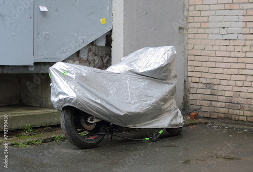 A motorcycle, covered with a cover from bad weather, stands near a white brick wall