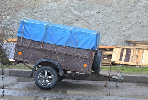 A small old rusty cargo trailer for a car stands near the wall