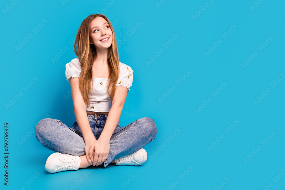 Full length portrait of lovely girl sit floor look empty space wear top isolated on blue color background Full length portrait of lovely girl sit floor look empty space wear top isolated on blue color background