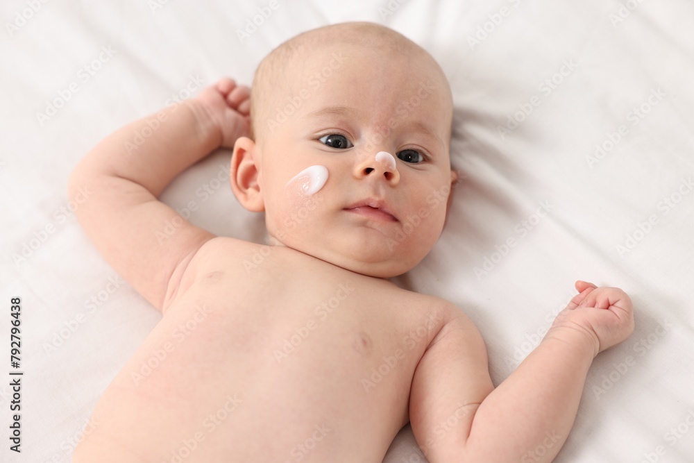 Cute little baby with cream on face on white blanket, above view