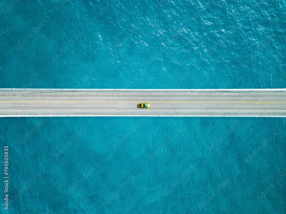 Aerial view of bridge road with yellow car over blue sea ocean