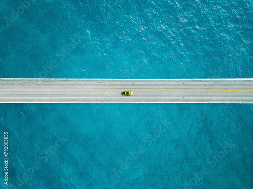 Aerial view of bridge road with yellow car over blue sea ocean