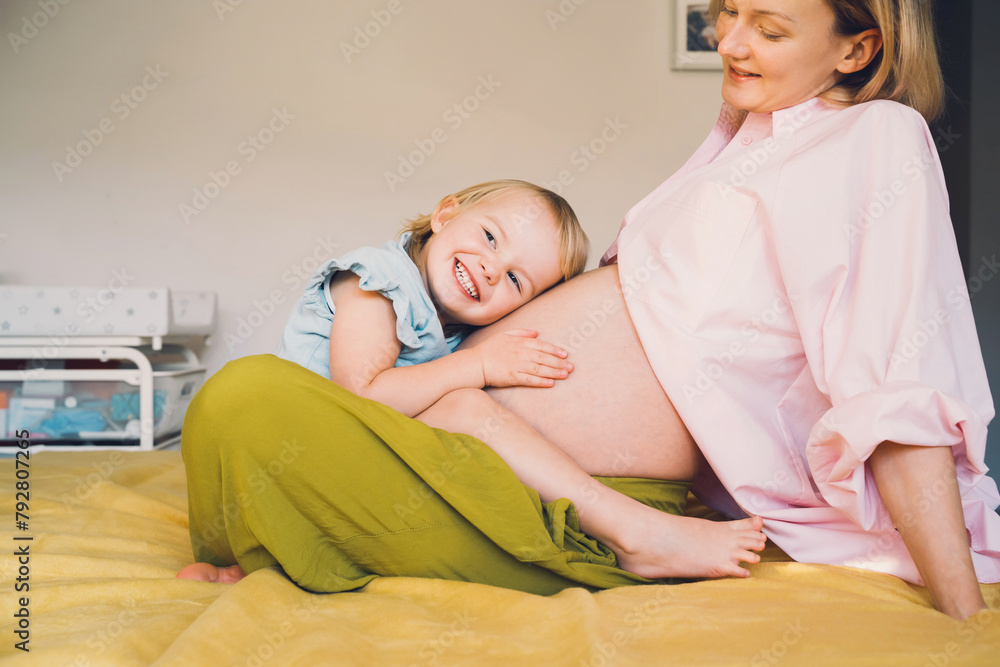 Pregnant mother and daughter together at home. Woman with her first child during second pregnancy. Motherhood and parenting concept. Toddler smiling girl and mom. Happy family expecting for new baby. Pregnant mother and daughter together at home. Woman with her first child during second pregnancy. Motherhood and parenting concept. Toddler smiling girl and mom. Happy family expecting for new baby.