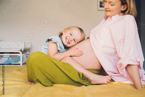 Pregnant mother and daughter together at home. Woman with her first child during second pregnancy. Motherhood and parenting concept. Toddler smiling girl and mom. Happy family expecting for new baby.