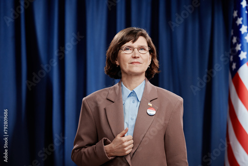 Mature brunette female candidate taking part in pre-election campaign looking at camera while standing against American flag