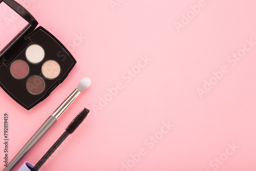 Colorful eyeshadow palette, makeup brush and black eyes mascara on light pink table background. Pastel color. Female beauty products. Closeup. Empty place for text. Top down view.