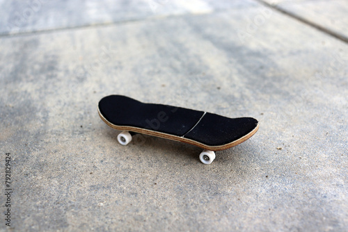 Blank wooden fingerboard at the ramp in concrete skatepark, close up. Mini skateboard, small skateboard deck