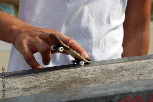 Male hand playing with black wooden fingerboard doing grind or slide trick at the ramp in skatepark, close up. Mini skateboard, small skateboard deck