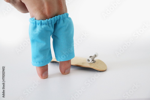 Male hand with miniature finger skate jeans short next to wooden fingerboard on the white background, close up. Mini skateboard, small skateboard deck