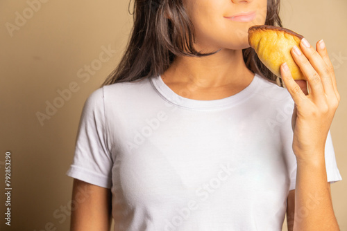 unrecognizable young woman dressed in a white shirt holding an empanada, salteña 
