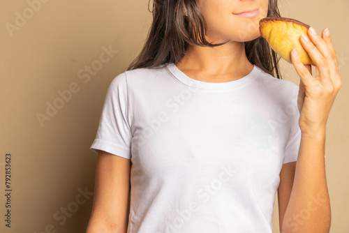 unrecognizable young woman approaching to bite into a snack, empanada, salteña, enjoying food happily
 photo