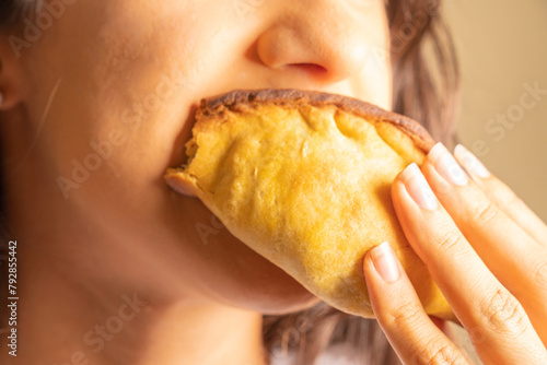 unrecognizable young woman biting into a snack, empanada, salteña, happily enjoying food
