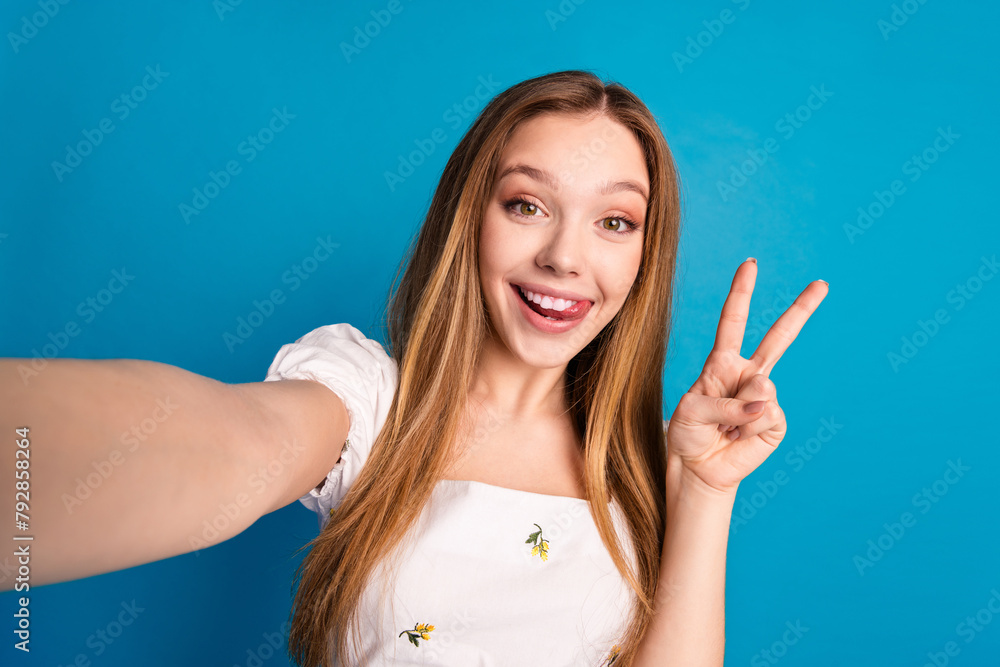 Photo of happy positive girl make selfie show v sign isolated blue color background Photo of happy positive girl make selfie show v sign isolated blue color background