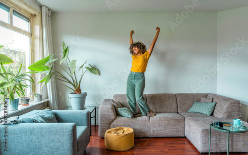 Happy afro american woman dancing on the sofa at home - Smiling girl enjoying day off lying on the couch - Healthy life style, good vibes people and new home concept