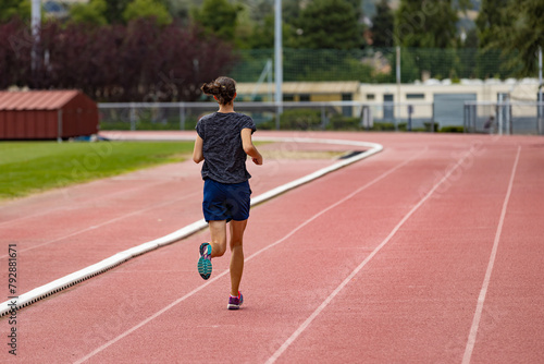 Back view of a young woman running on a stadium track; back view of a young athlete jogging on a running track