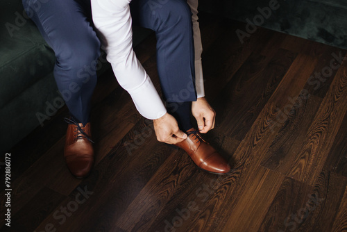 Brown leather shoe lacing. Businessman in white shirt and suit trousers. Groom getting ready for the wedding. Wearing clothes background. Dressing up male fashion. Business fashion hotel room.	
 photo