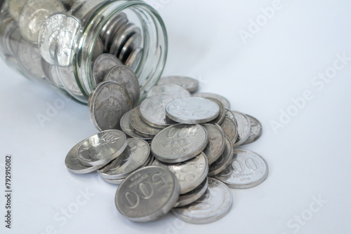 Glass jar of Indonesian Rupiah coins spilled on a white background. Coins in glass jar. Business and finance concept.