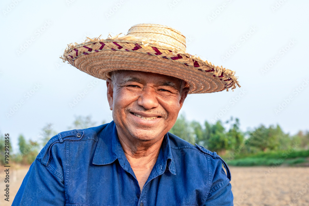 Happily smiling elderly farmer man in straw hat standing on agricultural area and looking at the camera, portrait, close-up