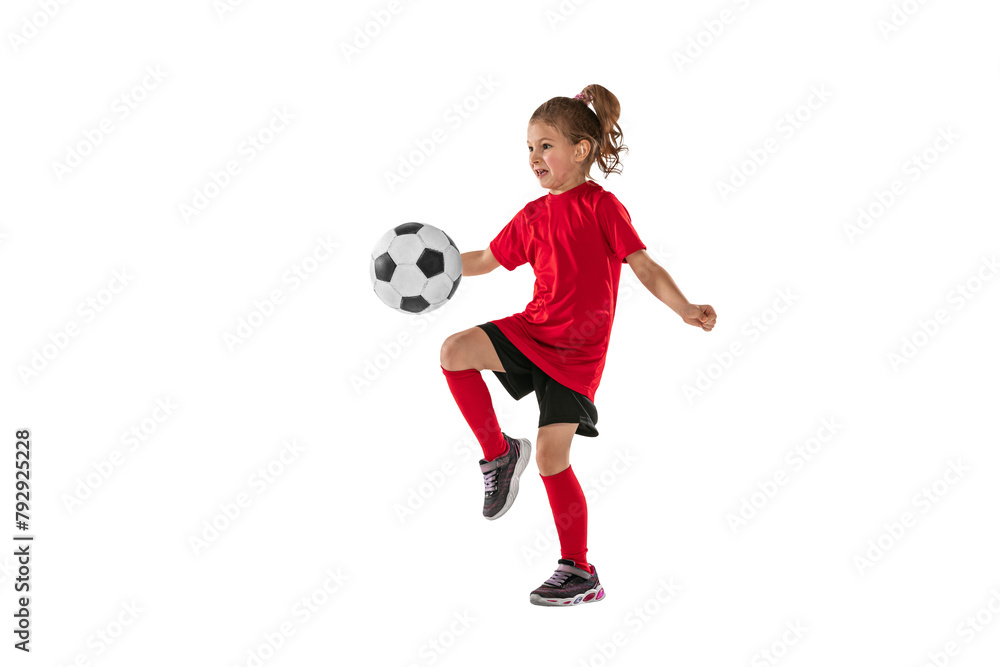 Portrait of girl, child, football player in red uniform training, kicking ball with knee against transparent background. Sportive and active kid. Concept of action, team sport game, energy, vitality.