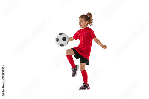 Portrait of girl, child, football player in red uniform training, kicking ball with knee against transparent background. Sportive and active kid. Concept of action, team sport game, energy, vitality. © Lustre