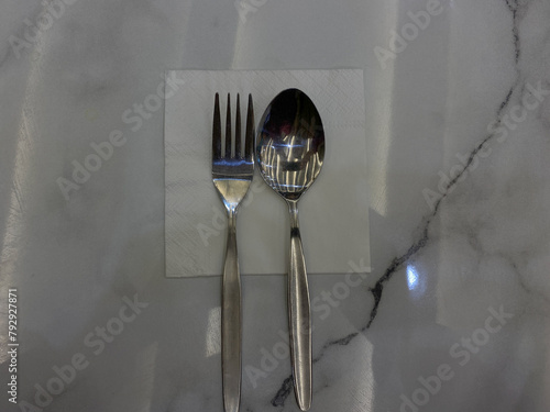 One set of stainless steel spoon and fork, on top of tissue, on the white table